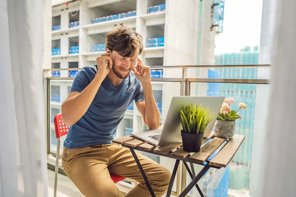 Man plugging his ears to avoid hearing airborn noise coming from outside of his apartment